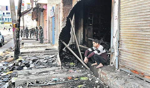Security forces are seen in a riot-hit street in northeast Delhi as a youth sits outside a gutted shop. ( Photo | Parveen Negi, EPS)