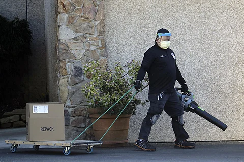 A worker at the Life Care Center in Kirkland, Wash., wears a mask and uses a leaf blower as he wheels a package on a cart. The nursing home is at the center of the outbreak of the coronavirus in Washington state. (Photo | AP)