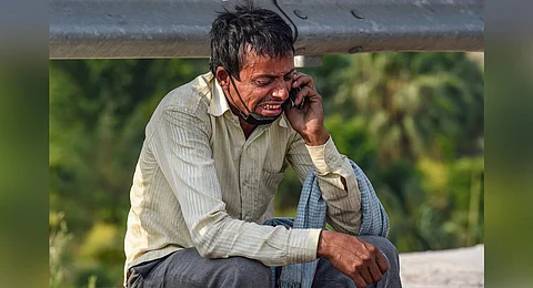 A migrant labourer reacts while talking to a relative over his mobile phone, at Nizamuddin Bridge in New Delhi, Monday, May 11, 2020, during ongoing COVID-19 lockdown. (Photo | PTI)