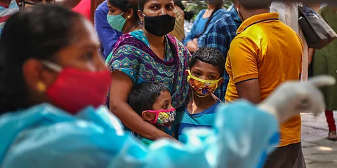 A woman holds on to two children as they wait their turn to get tested for COVID-19 in Hyderabad. (Photo| AP)