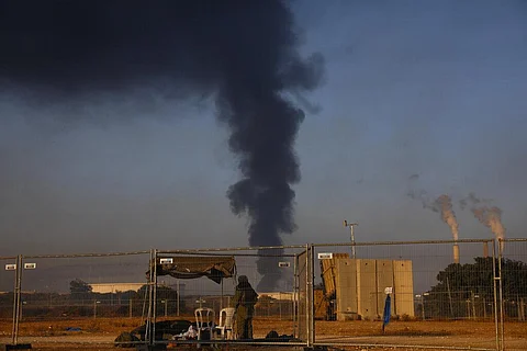 An Israeli soldier stands guard next to an Iron Dome air defense system as smoke rises from an oil tank on fire after it was hit by a rocket fired from Gaza Strip, near Ashkelon. (Photo | AP)