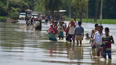 Villagers wade through a flooded road after heavy rainfall in Hojai district of Assam.