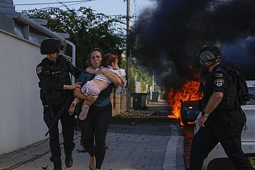 Police officers evacuate a woman and a child from a site hit by a rocket fired from the Gaza Strip, in Ashkelon, southern Israel, Saturday, Oct. 7, 2023. The rockets were fired as Hamas announced a new operation against Israel. (Photo | AP)