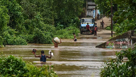 Residents of Kainmundi Village wade through a flooded road at Banki in Cuttack district of Odisha on August 3, 2023.
