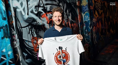 Martin Masser, ChangeNOW’s Director of Strategic Partnerships, holds a branded T-shirt in a graffiti-covered London passage.