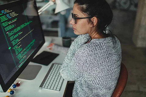 Photo of a young woman sitting at her desktop computer, doing computer programming in her home office