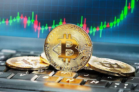 Bitcoins on keyboard with screen in the background displaying rising trend of its value