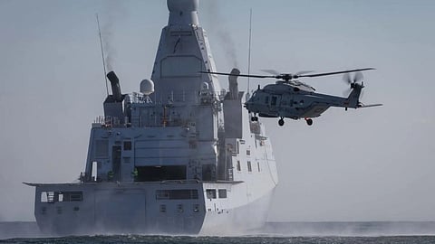 An NH90 helicopter hovers near the stern of the Royal Netherlands Navy offshore patrol vessel HNLMS Groningen.