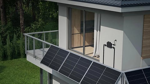 Two solar panels on a house balcony wired to a small microinverter on the wall.