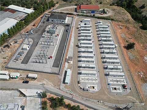 A utility-scale battery energy storage facility in Greece with rows of containerized BESS units, power conversion equipment and electrical infrastructure, set in a realistic Greek landscape.