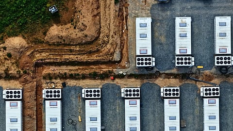 An aerial view of rows of containerised battery energy storage units with rooftop cooling systems on gravel pads at a site under construction, the asset class the RUPTL's roughly 6 GW standalone pipeline comprises.