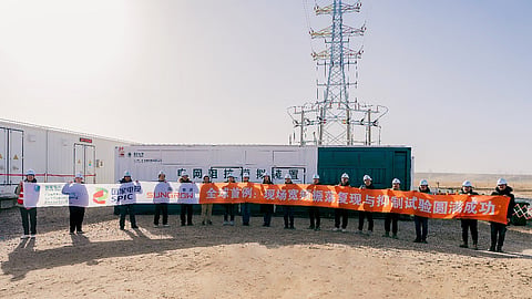 Team in hard hats holding banners beside equipment containers and a transmission tower in Qinghai.