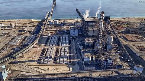 Aerial view of white battery container rows beside a coastal thermal power plant.
