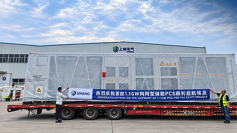 Two workers hold a shipment banner beside a wrapped PCS station on a flatbed truck.