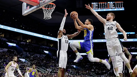 Warrior Stephen Curry drives against Spurs center LaMarcus Aldridge (12) and forward Davis Bertans (42) , in San Antonio, Monday, March 18, 2019. (AP Photo/Eric Gay)