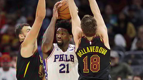 Philadelphia 76ers' Joel Embiid, center, squeezes between Cleveland Cavaliers' Ante Zizic, left and Matthew Dellavedova in the first half of an NBA basketball game, Wednesday, Feb. 26, 2020, in Cleveland.