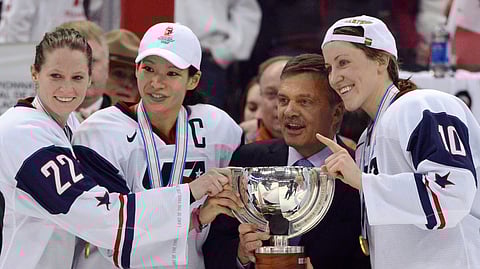 FILE - In this April 9, 2013, file photo, United States' Kacey Bellamy, Julie Chu and Meghan Duggan, from left, stand with IIHF president Rene Fasel as they are presented with the trophy after the U.S. team defeated Canada 3-2 in the gold medal game at the women's ice hockey world championships in Ottawa, Ontario. The women’s world hockey championships in Canada have been canceled because of the new coronavirus. International Ice Hockey Federation President René Fasel tells The Associated Press the decision was made by conference call Saturday, March 7, 2020. (Sean Kilpatrick/The Canadian Press via AP, File)