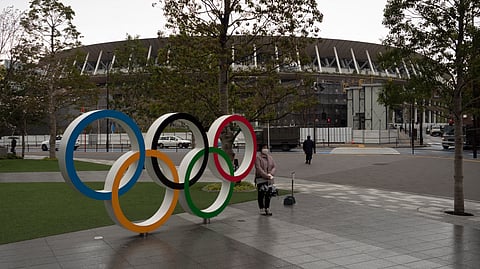 A woman pauses for photos next to the Olympic rings near the New National Stadium in Tokyo, Monday, March 23, 2020. The IOC will take up to four weeks to consider postponing the Tokyo Olympics amid mounting criticism of its handling of the coronavirus crisis that now includes a call for delay from the leader of track and field, the biggest sport at the games.