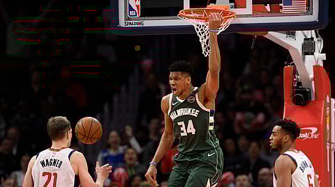 Milwaukee Bucks forward Giannis Antetokounmpo (34) hangs from the rim after his dunk during the second half of an NBA basketball game next to Washington Wizards forward Moritz Wagner (21) and forward Troy Brown Jr. (6) , Monday, Feb. 24, 2020, in Washington. (AP Photo/Nick Wass)