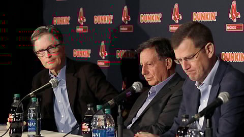 From left, in a Jan. 15, 2020, file photo, Boston Red Sox owner John Henry, chairman Tom Werner and CEO Sam Kennedy react during a news conference at Fenway Park in Boston. The Boston Red Sox were stripped of their second-round pick in this year’s amateur draft by Major League Baseball for breaking video rules in 2018 and former manager Alex Cora was suspended through the 2020 postseason for his conduct as bench coach with the Houston Astros the previous year.