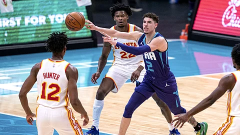 Charlotte Hornets guard LaMelo Ball (2) looks away while passing the ball past Atlanta Hawks forward De'Andre Hunter (12) and forward Cam Reddish (22) during the first half of an NBA basketball game in Charlotte, N.C., Saturday, Jan. 9, 2021.