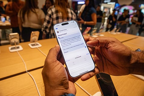 A person holds an Iphone displaying an email about dinner plans. The scene is inside a busy store with a wooden table and other phones on display.