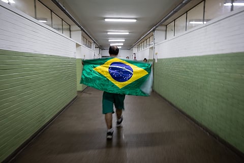 Brazilians Vote In Tightly Contested Presidential Race
A voter carries a Brazilian national flag at a polling station during the general election in Sao Paulo, Brazil, on Sunday, Oct. 4, 2026. Brazilians are headed to the polls Sunday in a tightly contested first round vote between an incumbent that is seeking a fourth term and the eldest son of former President Jair Bolsonaro. Photographer: Maira Erlich/Bloomberg via Getty Images