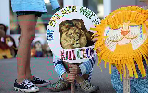 Piper Hoppe, 10, from Minnetonka, Minnesota, holds a sign at the doorway of River Bluff Dental clinic in protest against the killing of a famous lion in Zimbabwe, in Bloomington, Minnesota July 29, 2015. A Zimbabwean court on Wednesday charged a professional local hunter Theo Bronkhorst with failing to prevent an American from unlawfully killing 'Cecil', the southern African country's best-known lion. The American, Walter James Palmer, a Minnesota dentist who paid $50,000 to kill the lion, has left Zimbabwe. He says he did kill the animal but believed the hunt was legal and that the necessary permits had been issued. REUTERS/Eric Miller TPX IMAGES OF THE DAY