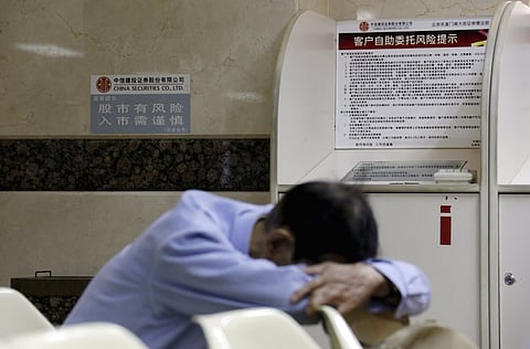 An investor takes a nap next to a sign (L) that reads "the stock market is risky, be prudent in investment" at a brokerage house in Beijing, August 26, 2015. Asian shares struggled on Wednesday as investors feared fresh rate cuts in China would not be enough to stabilise its slowing economy or halt a stock collapse that is wreaking havoc in global markets. REUTERS/Jason Lee