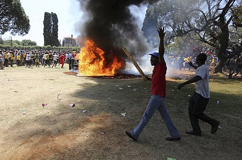 A demonstrator gestures in front of a burning portaloo during a protest over planned increases in tuition fees outside the Union building in Pretoria, South Africa October 23, 2015. South African police fired stun grenades at students who lit fires outside President Jacob Zuma's offices following a week of protests, the first signs of the post-apartheid 'Born Free' generation flexing its muscle. REUTERS/Siphiwe Sibeko