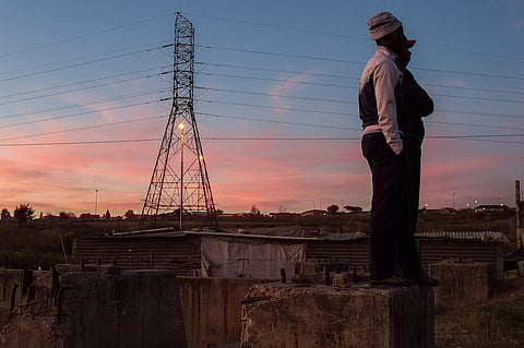 Residents of an informal settlement without power supplies watch the sun set beyond an electricity pylon in Soweto, South Africa, on Monday, May 25, 2015. Eskom Holdings SOC Ltd. is struggling to supply the country with enough electricity after 20 years of underinvestment in power plants and this year it has implemented the most rolling blackouts on record as it grapples to meet demand. Photographer: Dean Hutton/Bloomberg