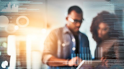 Defocused shot of two programmers using a digital tablet while working on a source code at night