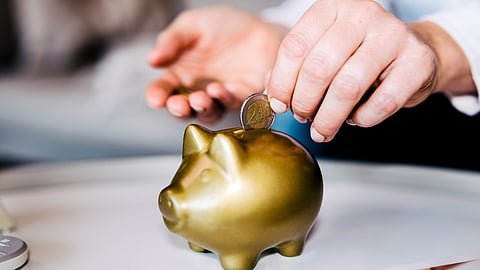 Woman putting savings in a golden piggy bank.