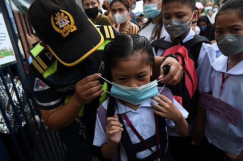 In this file photo, a city hall employee helps a student put on a face mask during the opening of classes at a school in Quezon City, suburban Manila on 22 August 2022. (Photo by Ted ALJIBE / AFP)