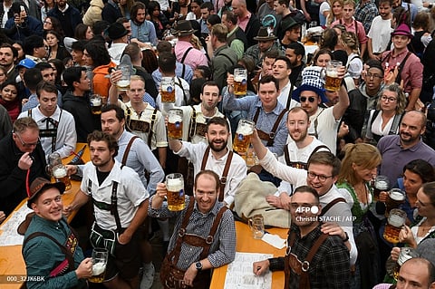 Visitors hold up their beer mugs as they celebrate during the opening of the Oktoberfest beer festival at the Theresienwiese fair grounds in Munich, southern Germany, on September 17, 2022. - The world renowned Beer festival is to take place from September 17 to October 3, 2022 without access restrictions, after the past two years' editions had been cancelled due to the coronavirus pandemic. (Photo by Christof STACHE / AFP)