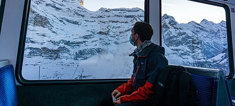 This young man traveling through the Swiss Alps by train during pandemic times dons a mask for Covid-19 protection. | Photograph courtesy of UN