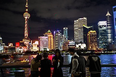 People visit the Bund promenade along the Huangpu River with the financial district of Lujiazui in the background in Shanghai, on 12 October 2022. (Photo by HECTOR RETAMAL / AFP)
