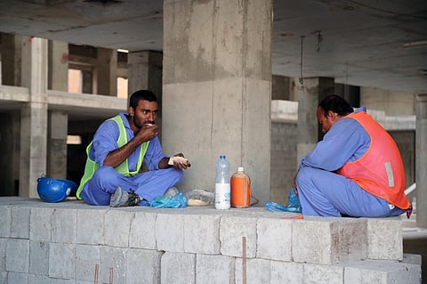In this file photo, migrant workers eat during a break at a construction site in the Qatari capital Doha. (Photo by STRINGER / AFP)