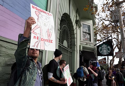 Striking Starbucks worker Ivan Vargas (left) holds a sign outside of a Starbucks coffee shop during a national strike on 17 November 2022 in San Francisco, California. Thousands of members of the Starbucks Workers Union are striking at over 100 Starbucks stores across the country as workers try to negotiate a contract with Starbucks. (Photo by JUSTIN SULLIVAN / GETTY IMAGES NORTH AMERICA / Getty Images via AFP)
