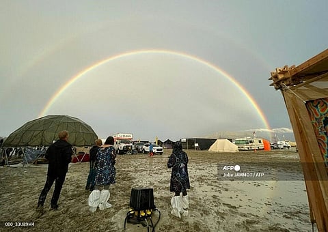 Attendees look at a double rainbow over flooding on a desert plain on September 1, 2023, after heavy rains turned the annual Burning Man festival site in Nevadas Black Rock desert into a mud pit. Tens of thousands of drenched festivalgoers were stranded on September 3, 2023, in deep, sticky mud in the Nevada desert after torrential rain turned the annual Burning Man gathering into a quagmire. All events at the counterculture festival, which drew some 70,000 people, were canceled after rain tore down structures for dance parties, art installations and other eclectic entertainment. (Photo by Julie JAMMOT / AFP)