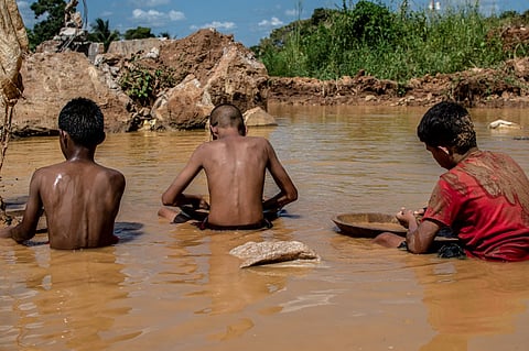 Venezuelan mining children work in a puddle of water and mud while searching for gold in an open pit mine in El Peru community, El Callao, Bolivar State, Venezuela, on 2 September 2023. (Photo by Yris PAUL / AFP)