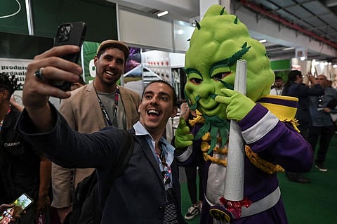 A visitor takes a selfie picture with a person in a costume of a cola of a cannabis plant during the Cannabis Expo Brazil, a hemp and cannabis industry exhibition, in Sao Paulo, Brazil, on 15 September 2023. (Photo by Nelson ALMEIDA / AFP)