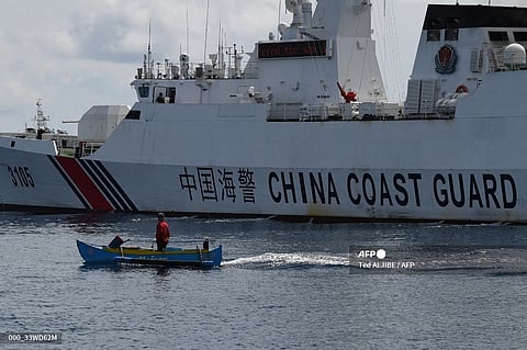 FILE PHOTO: This photo taken on 22 September 2023 shows a wooden boat, with Philippine fisherman Arnel Satam on board, drawfed by a Chinese coast guard vessel after he was intercepted for attempting to enter Scarborough Shoal in disputed waters of the South China Sea. In a high-seas chase lasting several minutes, Satam tries in vain to outrun the faster boats and slip inside the ring of reefs controlled by China, where fish are more abundant. The fishermen complained that China's actions at Scarborough Shoal were robbing them of a key source of income and a place to shelter safely during a storm. (Photo by Ted ALJIBE / AFP)