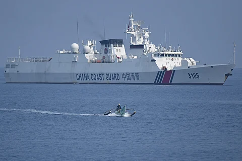FILE: This photo taken on September 20, 2023 shows a Philippine fisherman aboard his wooden boat sailing past a Chinese coast guard ship near the Chinese-controlled Scarborough Shoal in disputed waters of the South China Sea. China, which claims sovereignty over almost the entire South China Sea, snatched control of Scarborough Shoal from the Philippines in 2012. Since then, it has deployed coast guard and other vessels to block or restrict access to the fishing ground that has been tapped by generations of Filipinos. (Photo by Ted ALJIBE / AFP)
