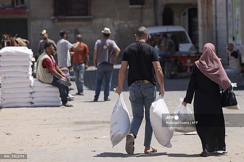 Palestinians carry carry their share of food aid provided to poor families at the United Nations Relief and Works Agency for Palestine Refugees (UNRWA) distribution center, in the Al-Shati refugee camp in Gaza city on June 5, 2023. (Photo by Mahmud Hams / AFP)