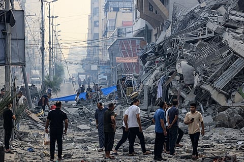 Residents walk along a debris-strewn street in front of a building that collapse during an Israeli air strike in Gaza City early on 8 October 2023. Photo by MAHMUD HAMS / AFP.