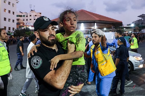 EDITORS NOTE: Graphic content / A member of the Palestinian security forces carries a child, wounded by Israeli airstrikes, into Al-Shifa hospital in Gaza City on October 11, 2023. Israel on October 11 kept up its bombardment of Hamas targets in the Gaza Strip, as Prime Minister Benjamin Netanyahu and a political rival announced an emergency government for the duration of the conflict that has already killed thousands. (Photo by Mohammed ABED / AFP)