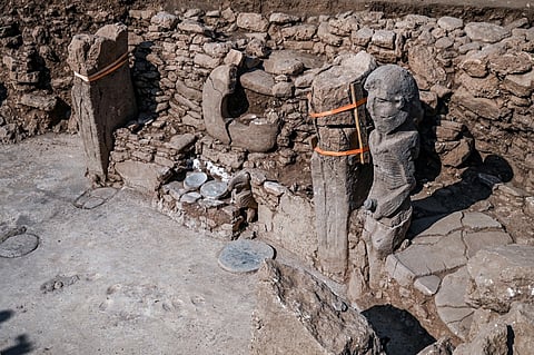 A photograph taken on 9 October 2023 at the archaeological site of Karahantepe in Sanliurfa, southeastern Turkey, shows newly found 2.3-meter high human statue (R), a stone man seated, clutching his sex with both hands, a vulture at his feet on the wall of a room. On this archaeological site, a stone statue, over 2.30 m high and seated on a bench adorned with a leopard, was discovered at the end of September in south-east Turkey, at the heart of a complex of some twenty sites that were home to thousands of humans during the Stone Age, twelve thousand years ago. (Photo by Ozan KOSE / AFP)