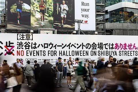People wait in front of a board reading "No events for Halloween on Shibuya streets" at Shibuya Crossing, one of the busiest intersections in the world, as local government asking public to refrain from celebrating Halloween there, in the Shibuya district of Tokyo on 27 October 2023. (Photo by Philip FONG / AFP)