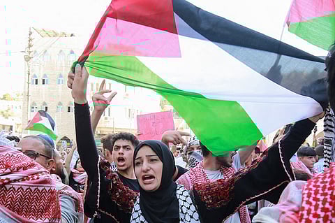 A demonstrator waves the Palestinian flag during a demonstration in Amman on 13 October 2023. Thousands of protesters poured onto the streets of several Middle East capitals in support of Palestinians amid Israeli air strikes on Gaza in reprisal for a surprise Hamas attack. (Photo by Khalil MAZRAAWI / AFP)